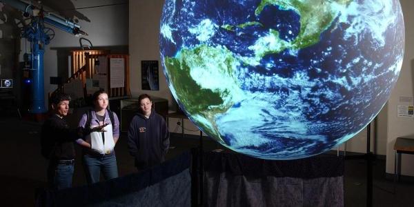 Students looking at lighted globe or Earth