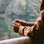 Arms rest over an outdoor railing, hands clutched.